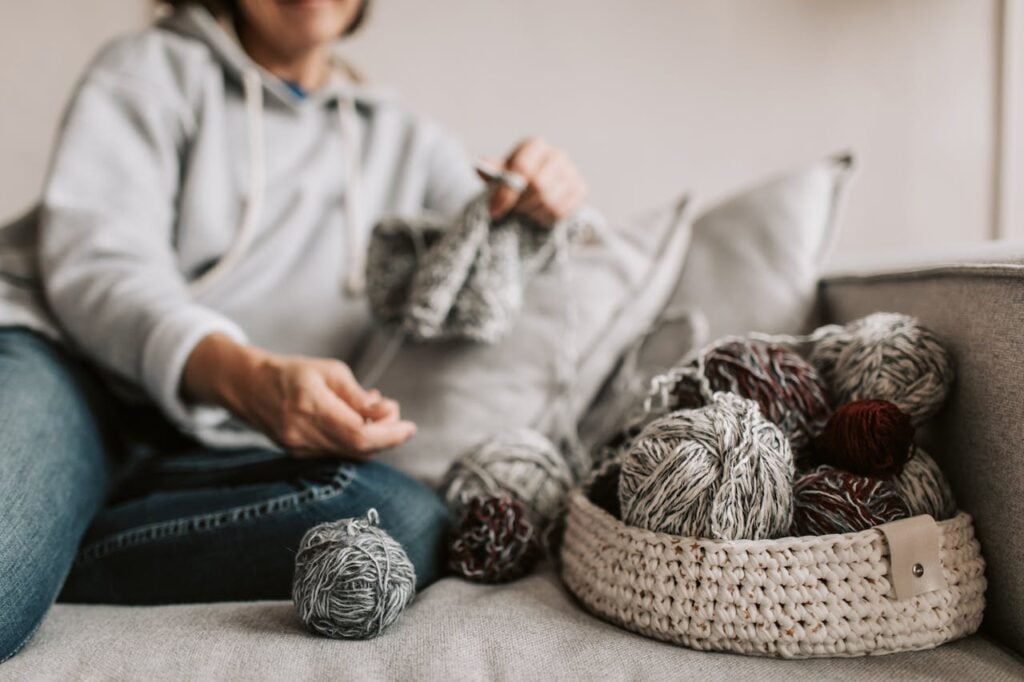 Balls of Yarn in a Woven Basket Beside a Woman Knitting